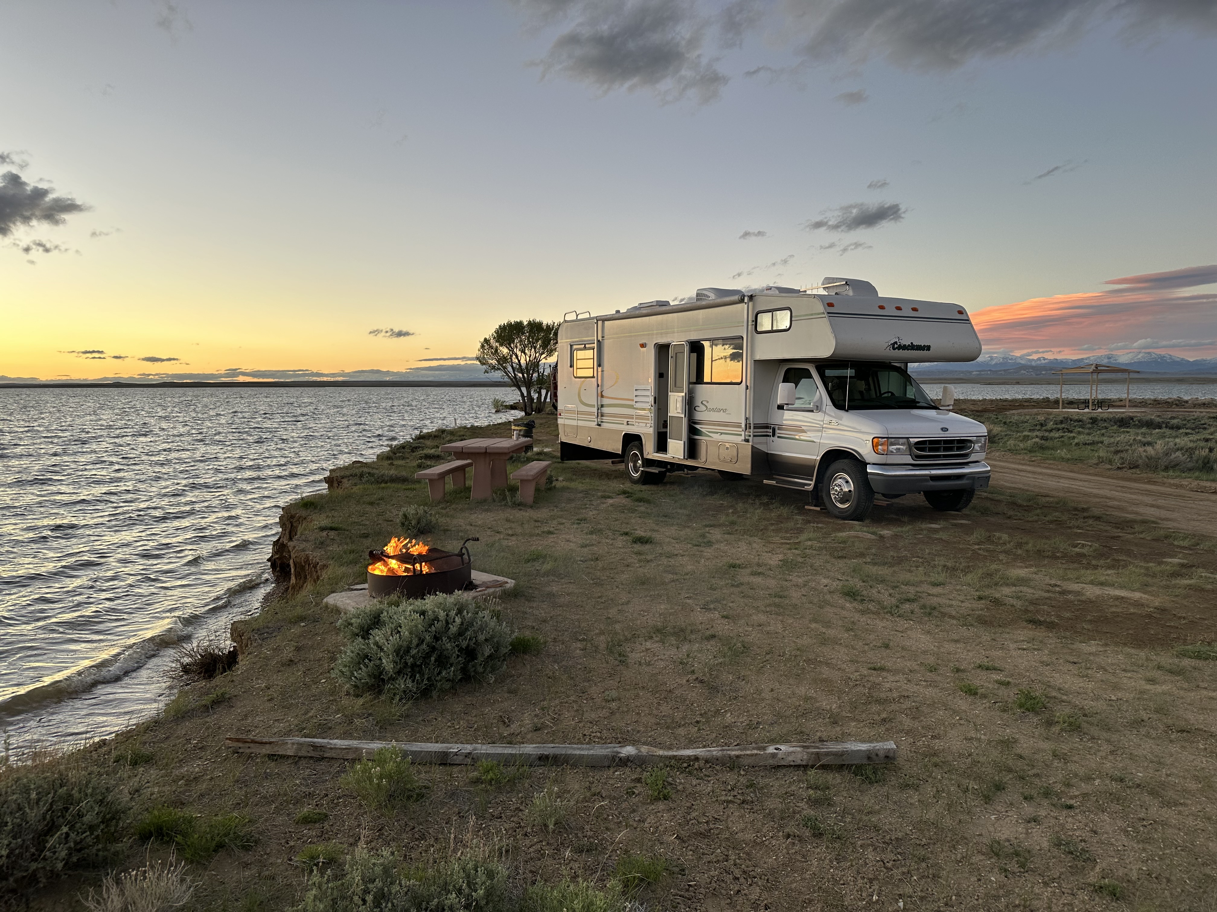 The renovated Class C RV parked at a lakeside campsite at sunset